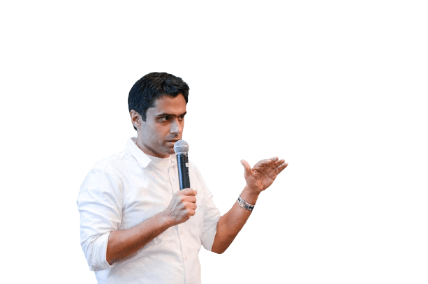 A man in a white shirt speaking into a microphone, using his other hand to gesture.