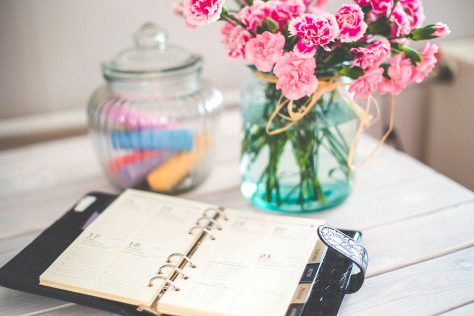 Open ring-bound planner on a desk beside a vase of carnations